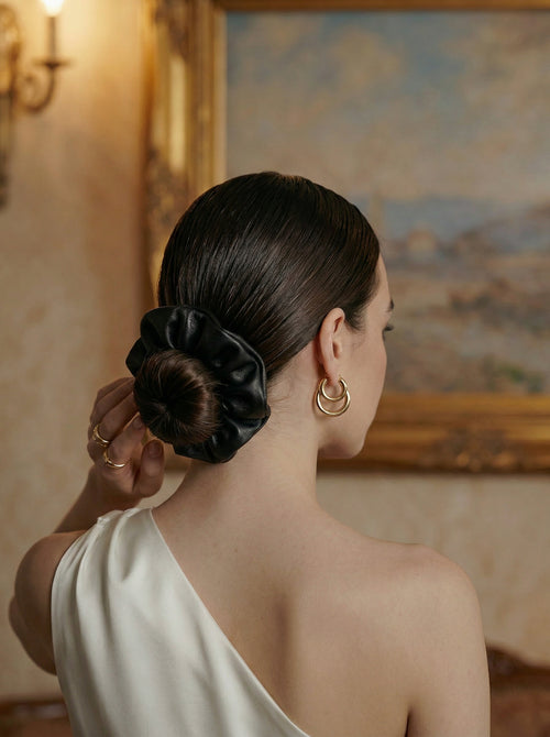 Woman with a black leather hair scrunchie and gold earrings in an elegant room.