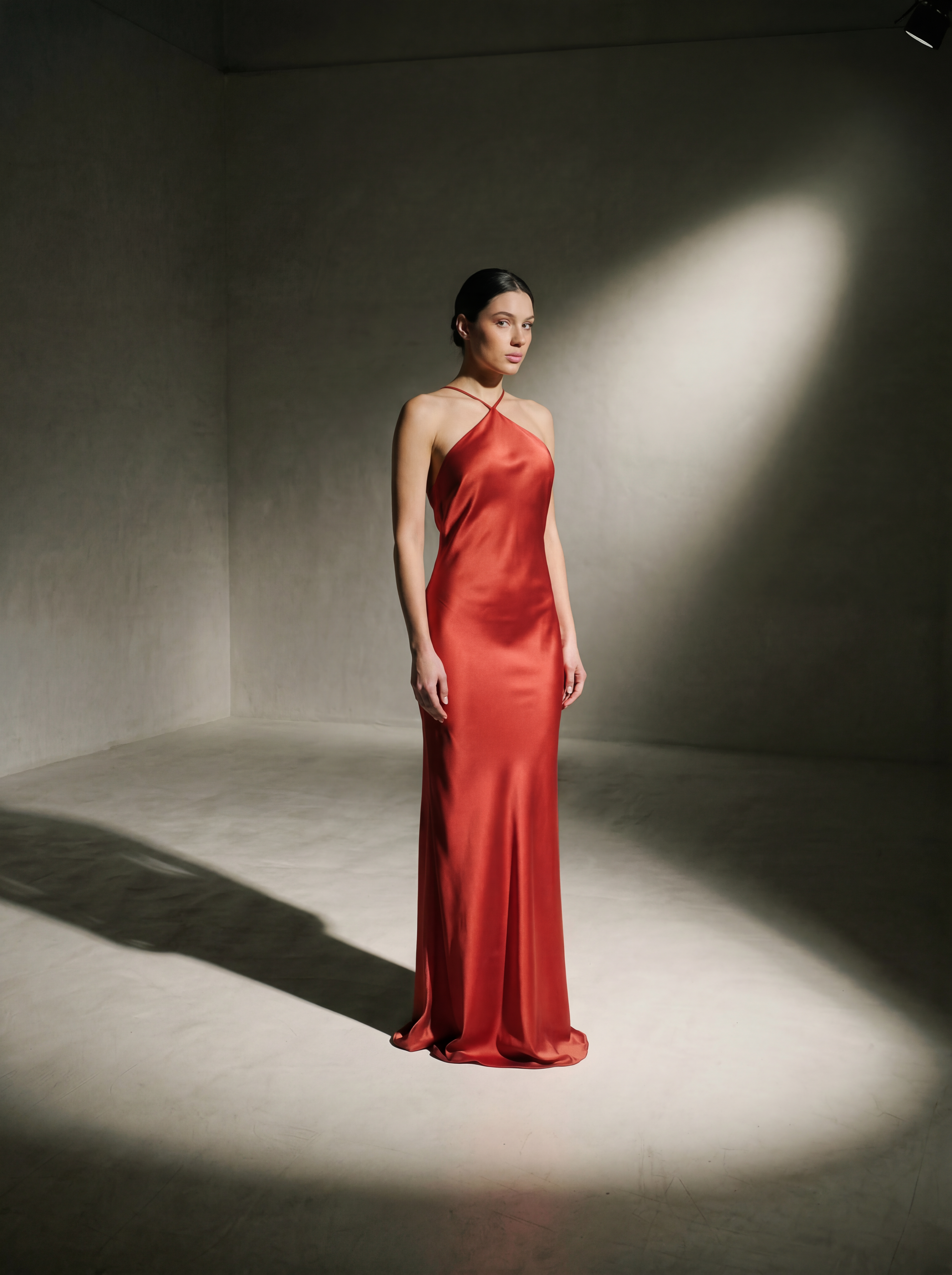 Woman in a red evening gown standing in a spotlight against a plain background