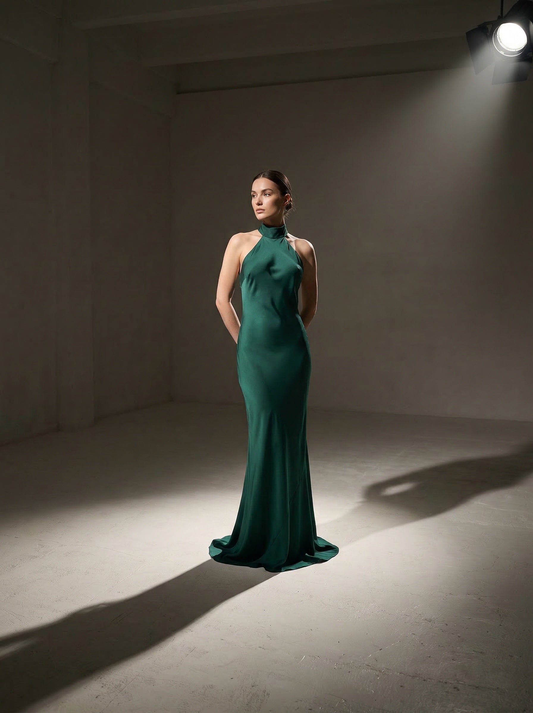 Woman in a pine green silk evening gown standing in a spotlight against a plain background