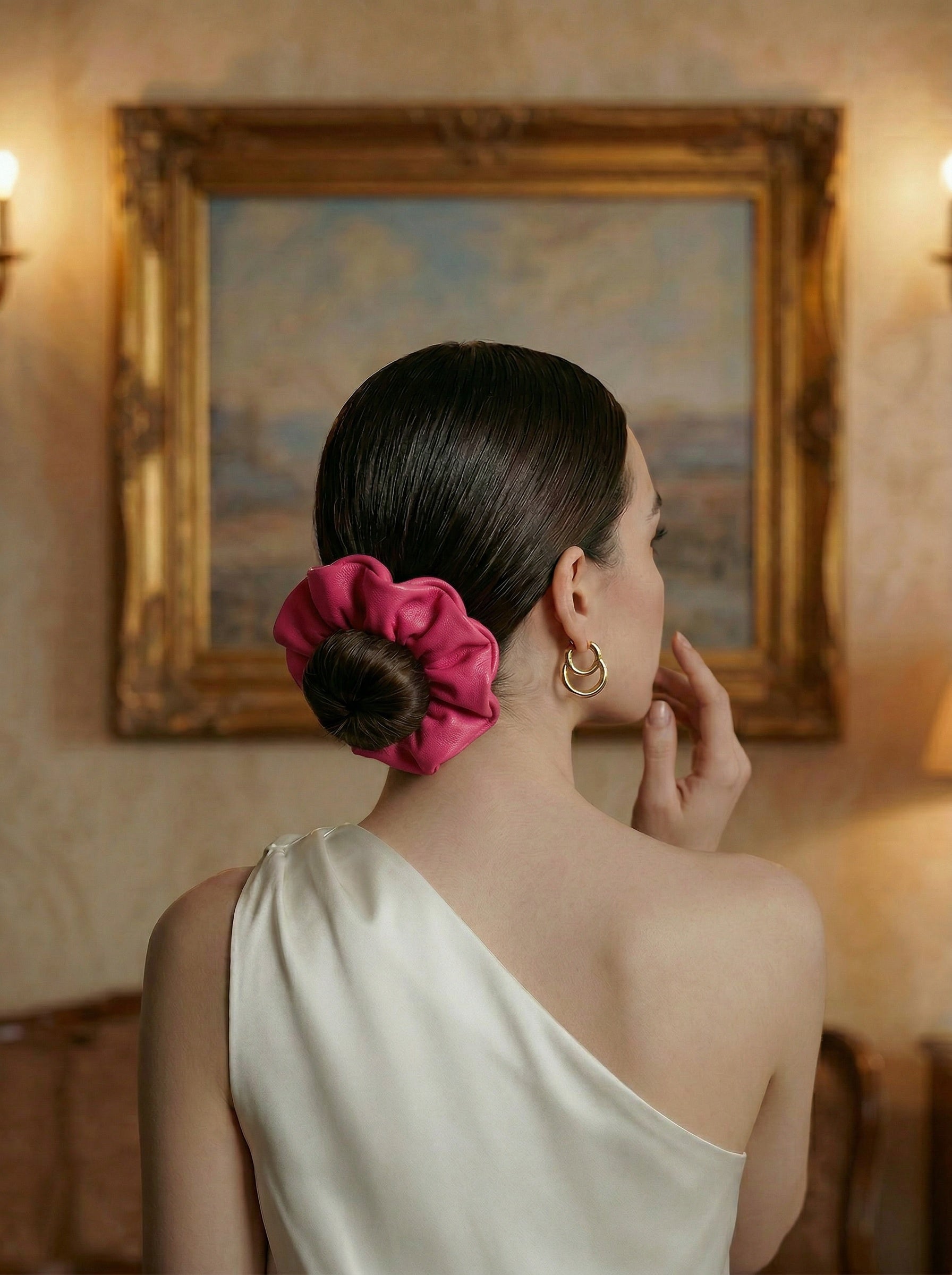 Woman with a pink leather scrunchie in her hair, standing in a room with a painting on the wall.