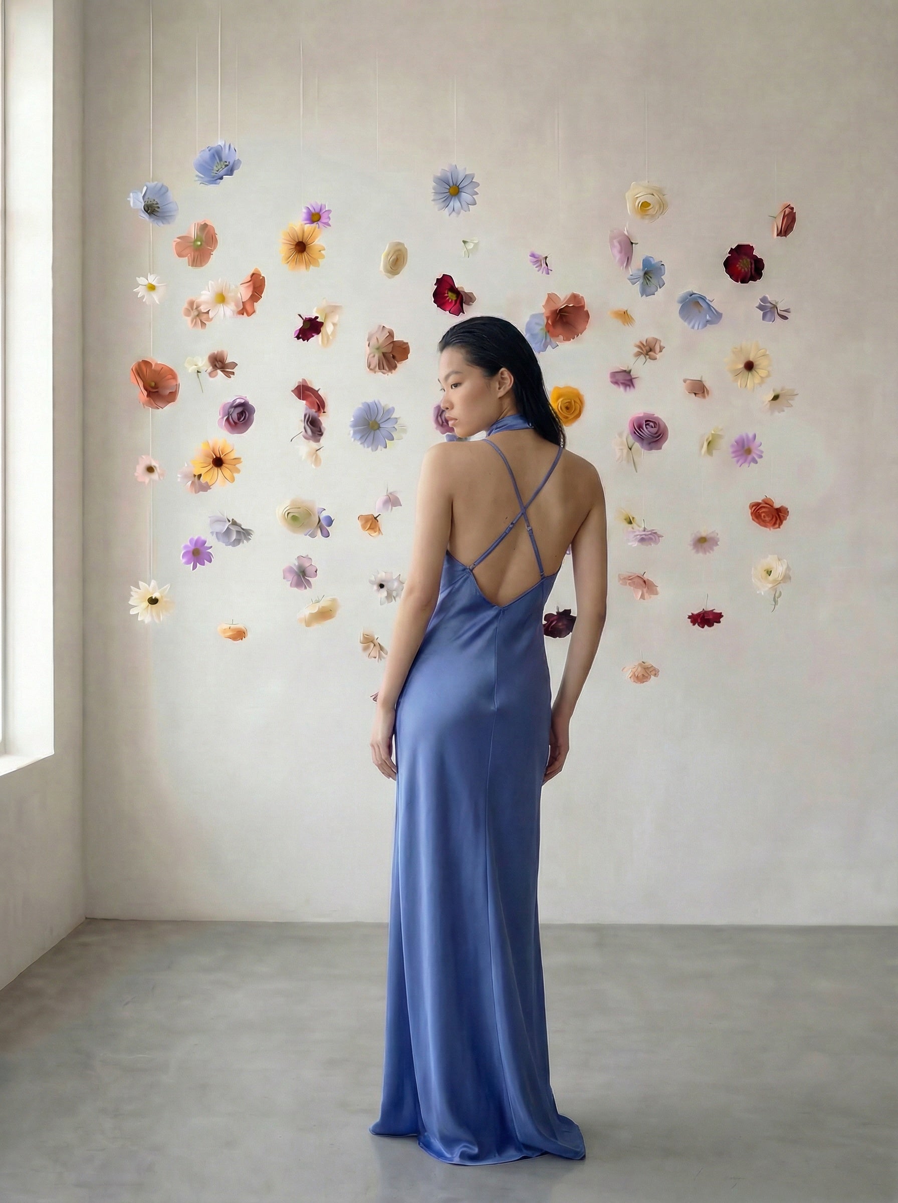 Woman in a blue dress standing in front of a wall with colorful flowers.