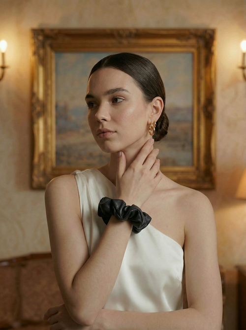 Woman in a white dress with a black scrunchie, standing in a room with a painting in the background.