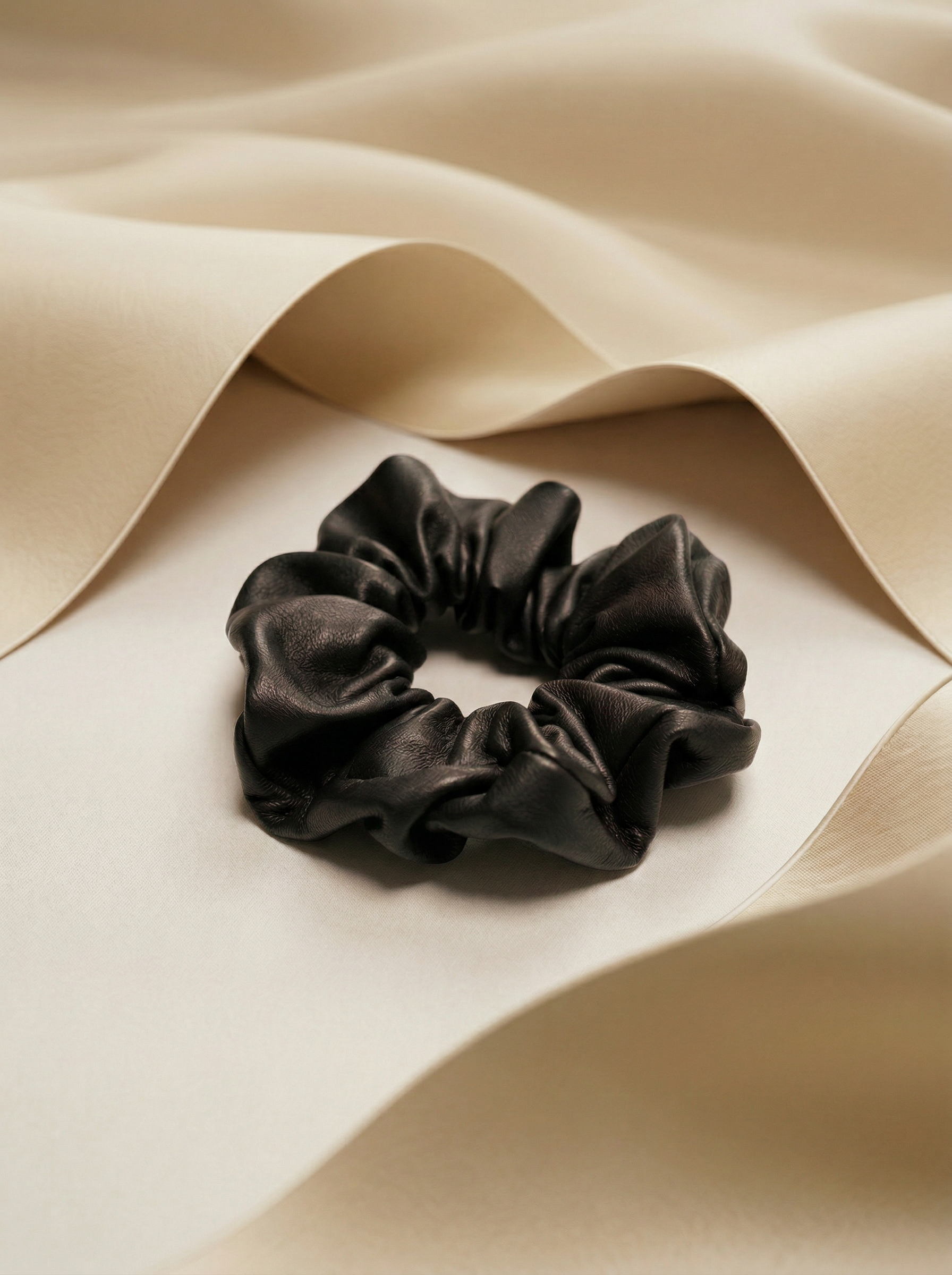 Black leather scrunchie next to beige silk fabric