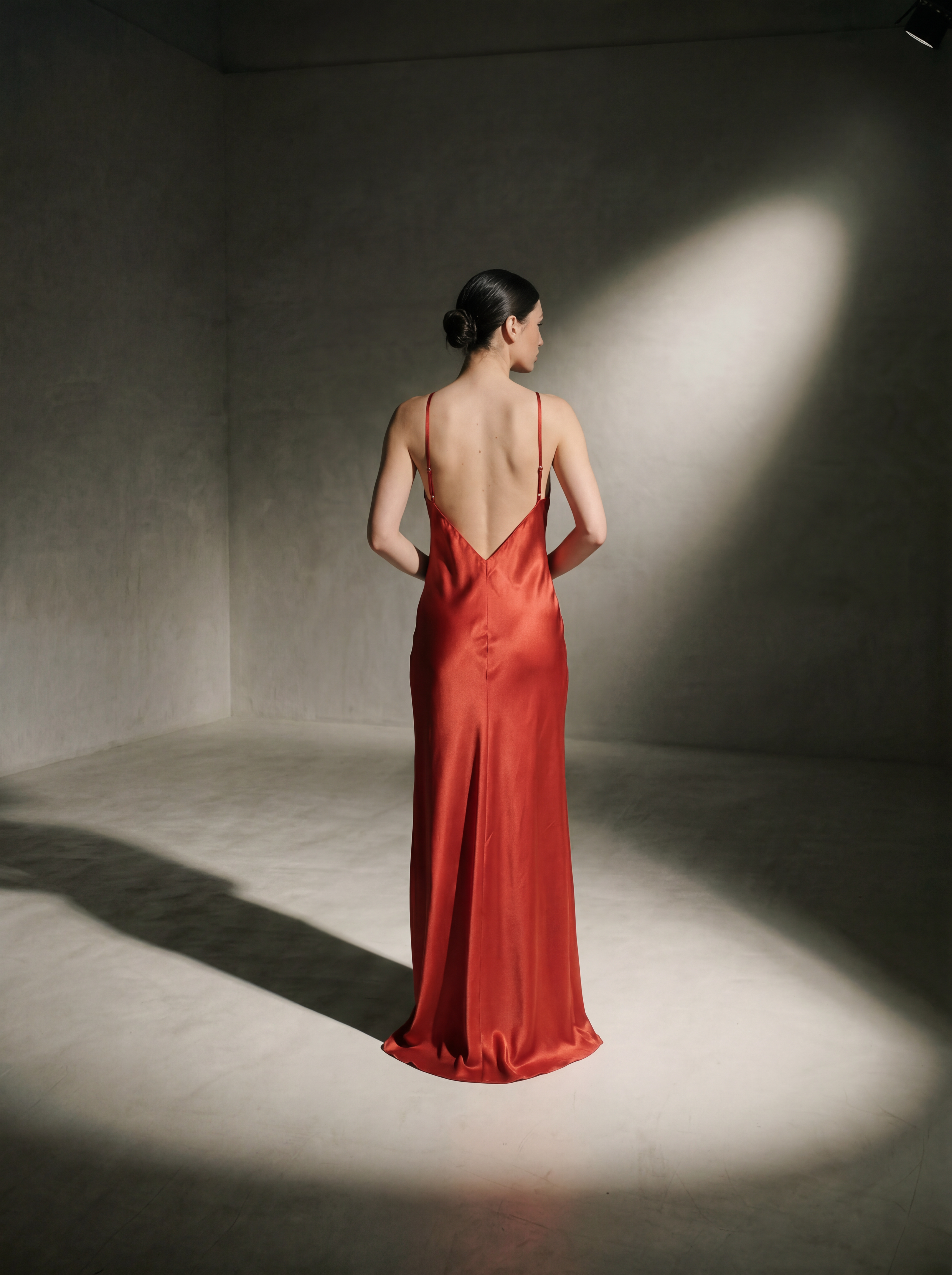 Woman in a red evening gown standing in a dimly lit room with a spotlight.