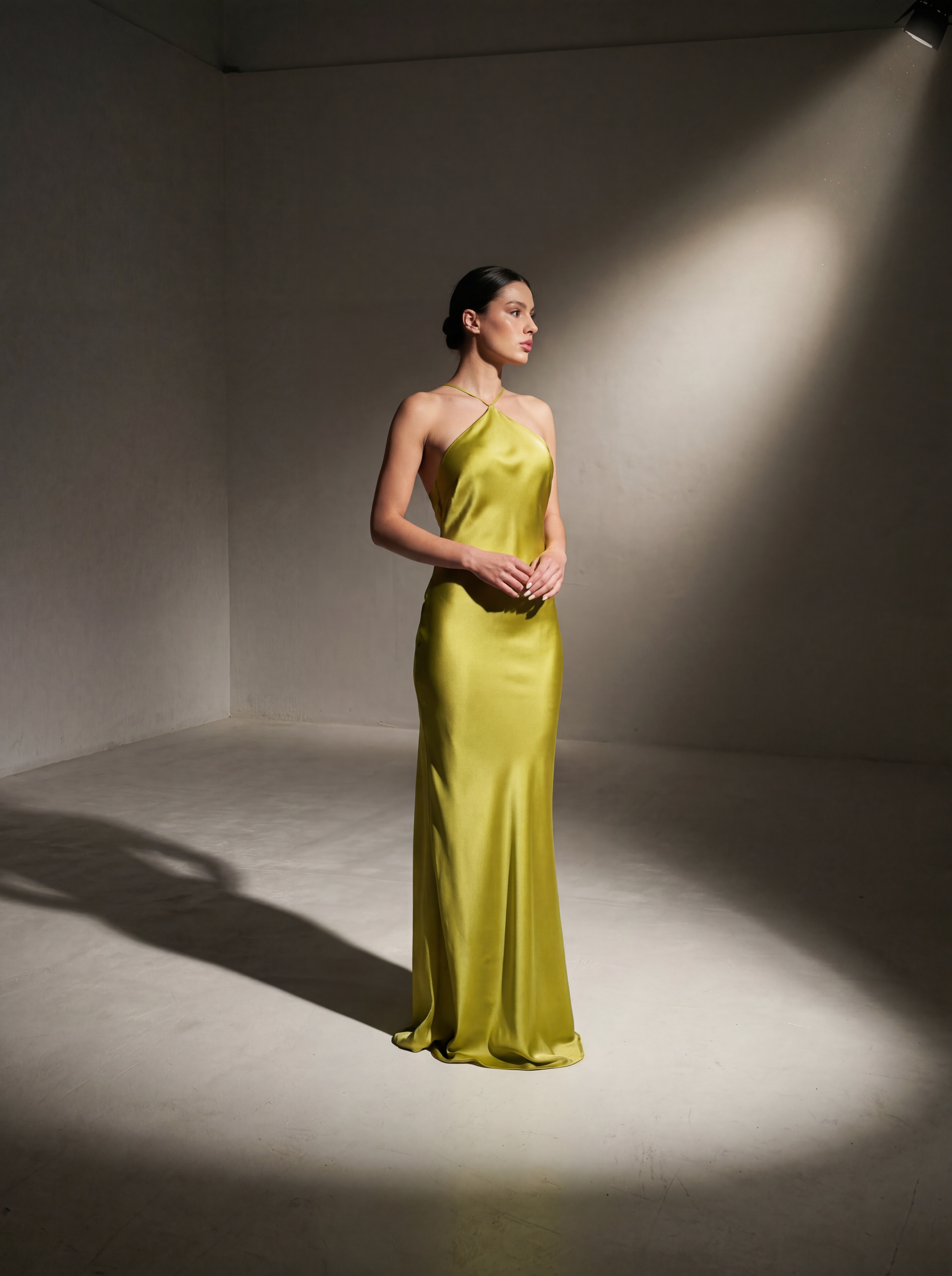 Woman wearing a yellow evening gown standing in a spotlight against a plain background