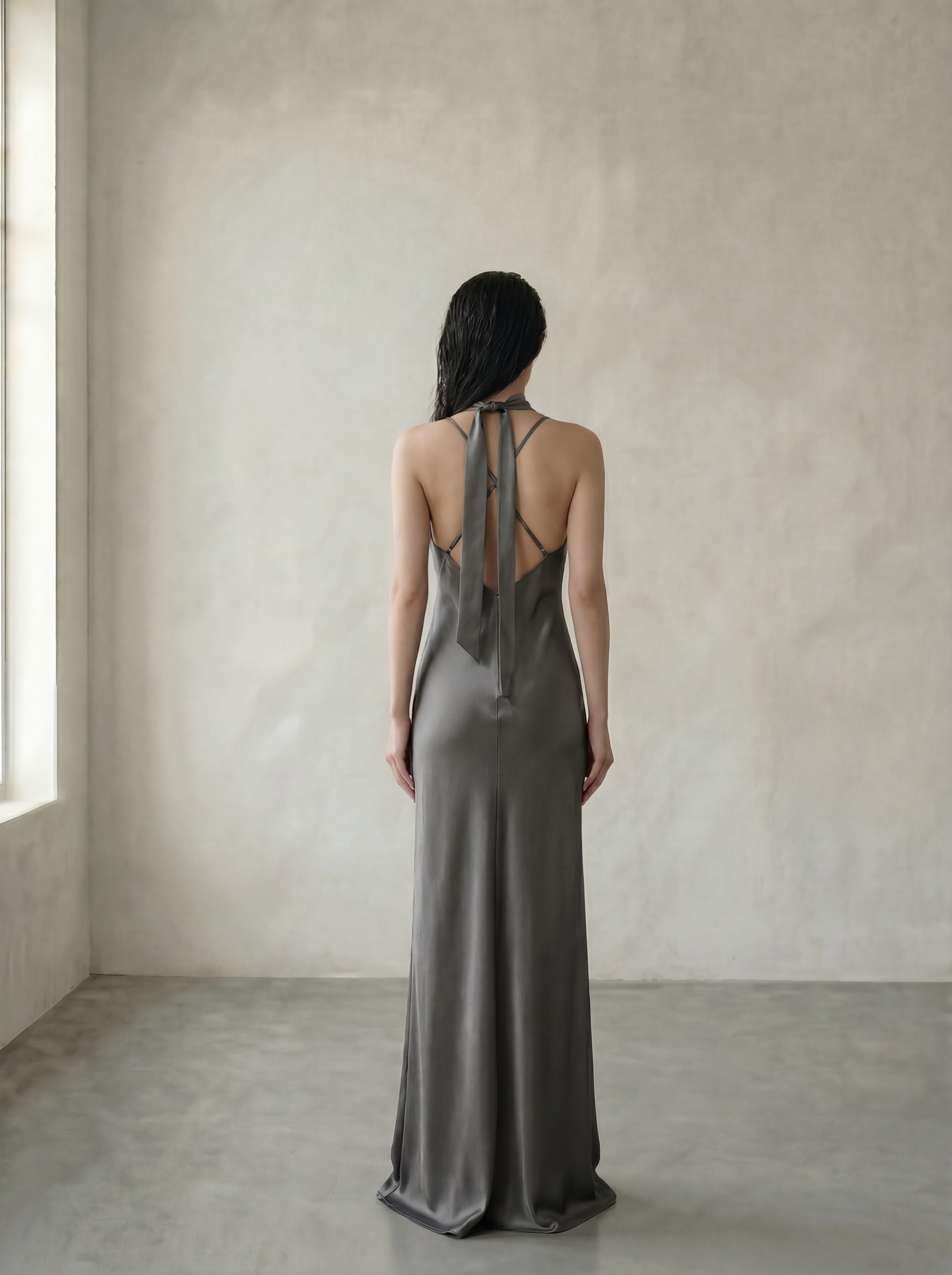 Woman wearing a gray dress with an open back in a minimalistic room.