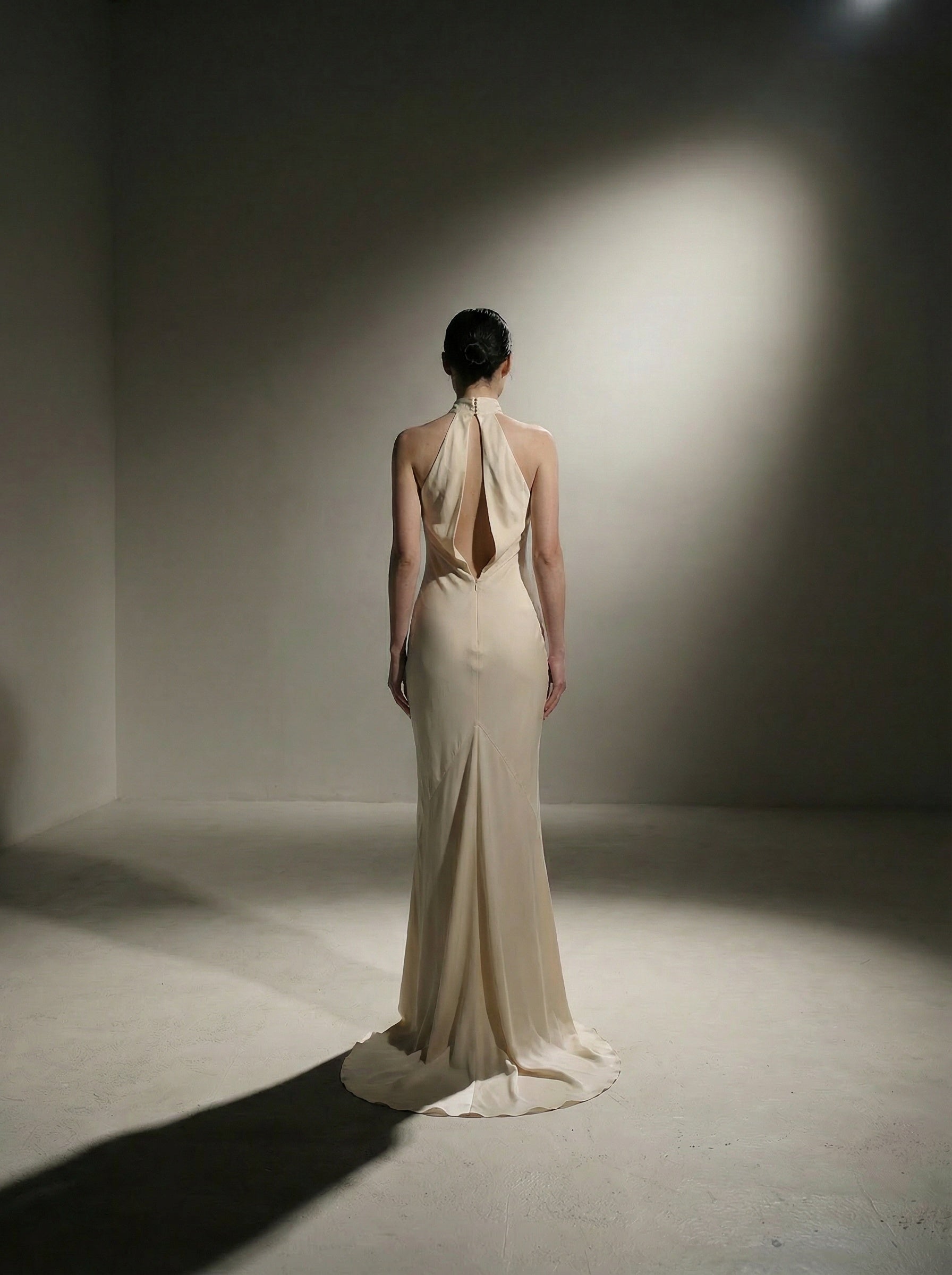 Woman in a white silk evening gown standing in a spotlight against a plain background