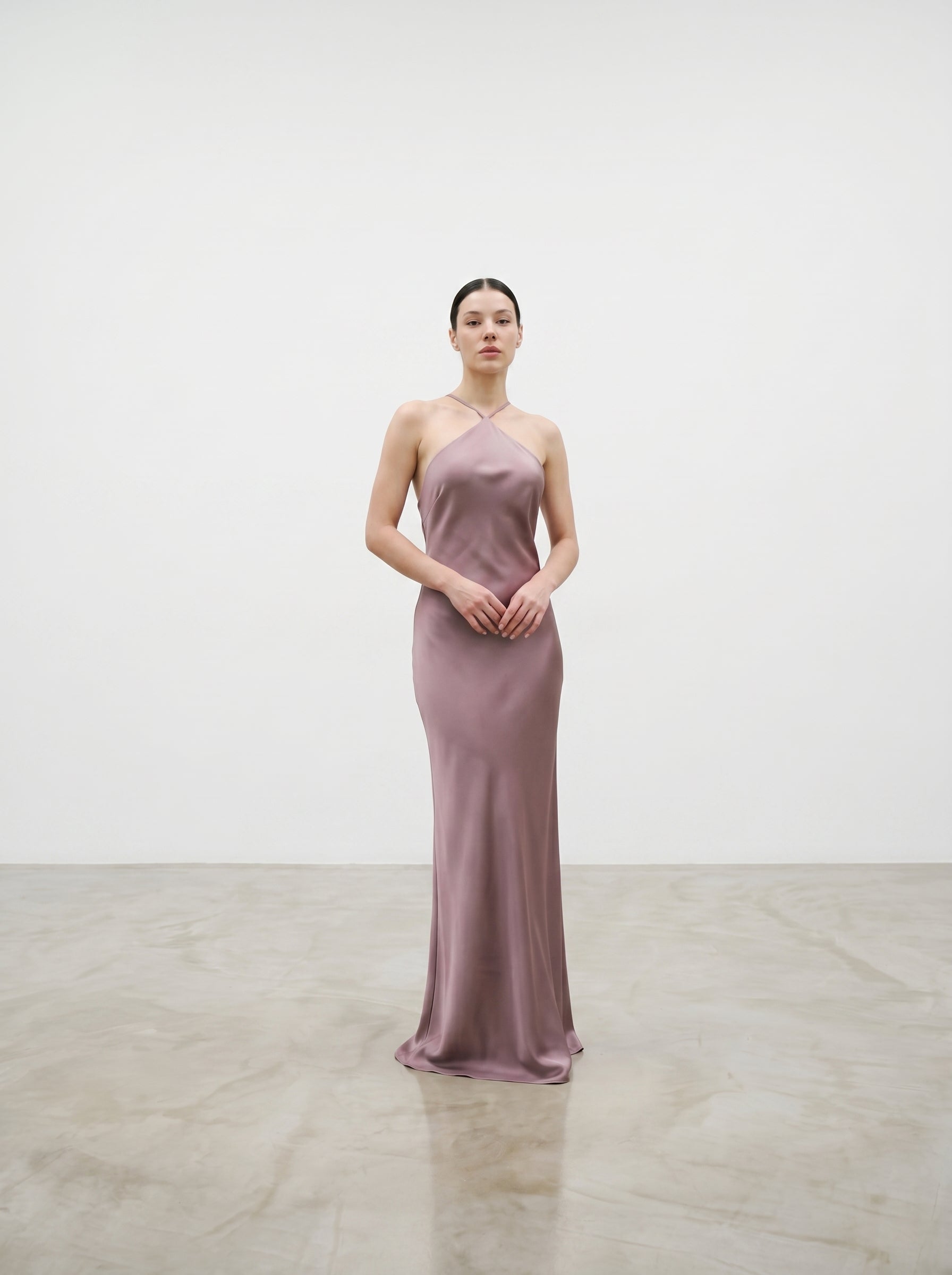 Woman in a pink satin gown standing in a spotlight against a plain background