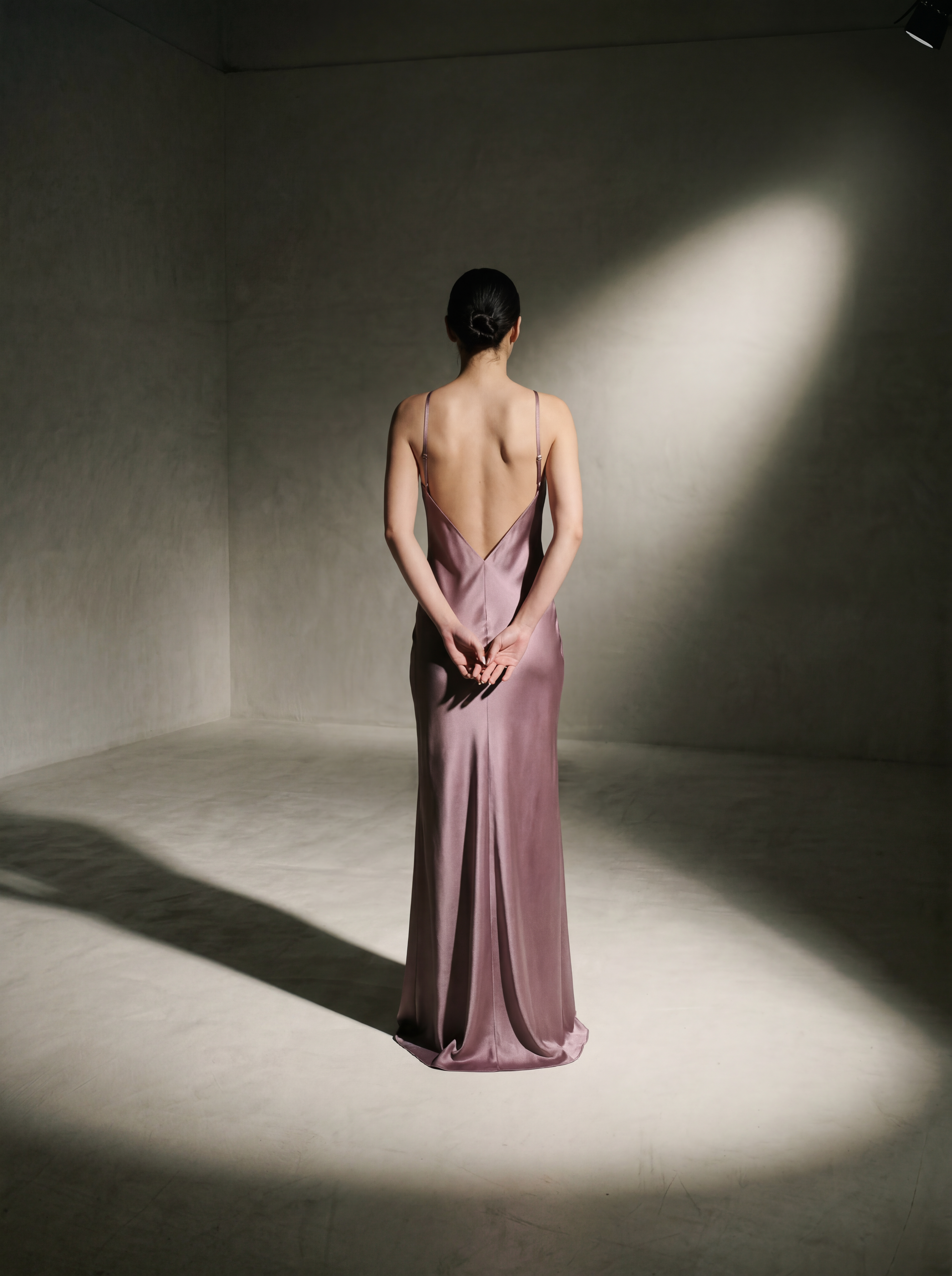 Woman in a backless pink gown standing in a softly lit room.