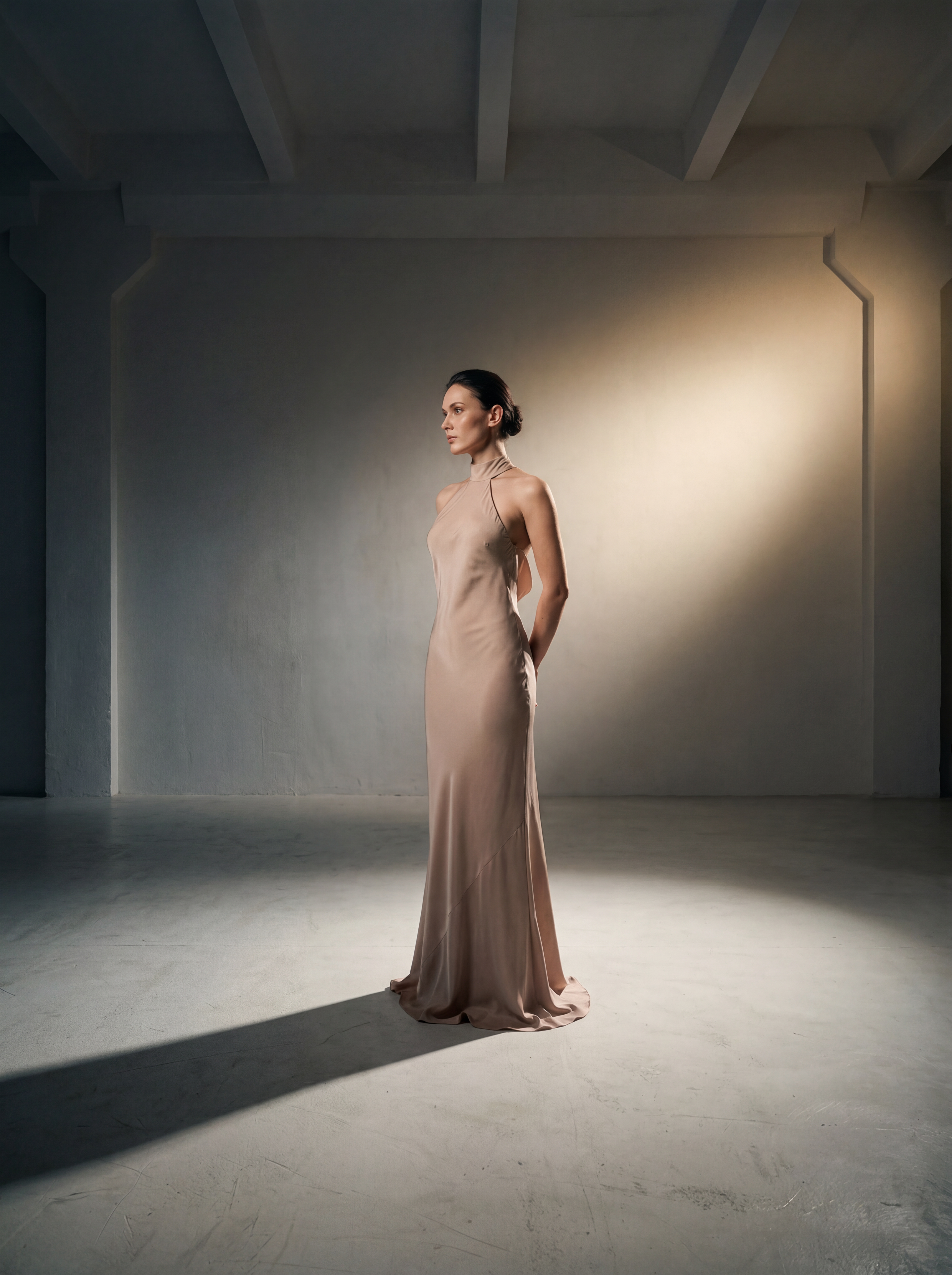 Woman in a beige evening gown standing in a softly lit room.