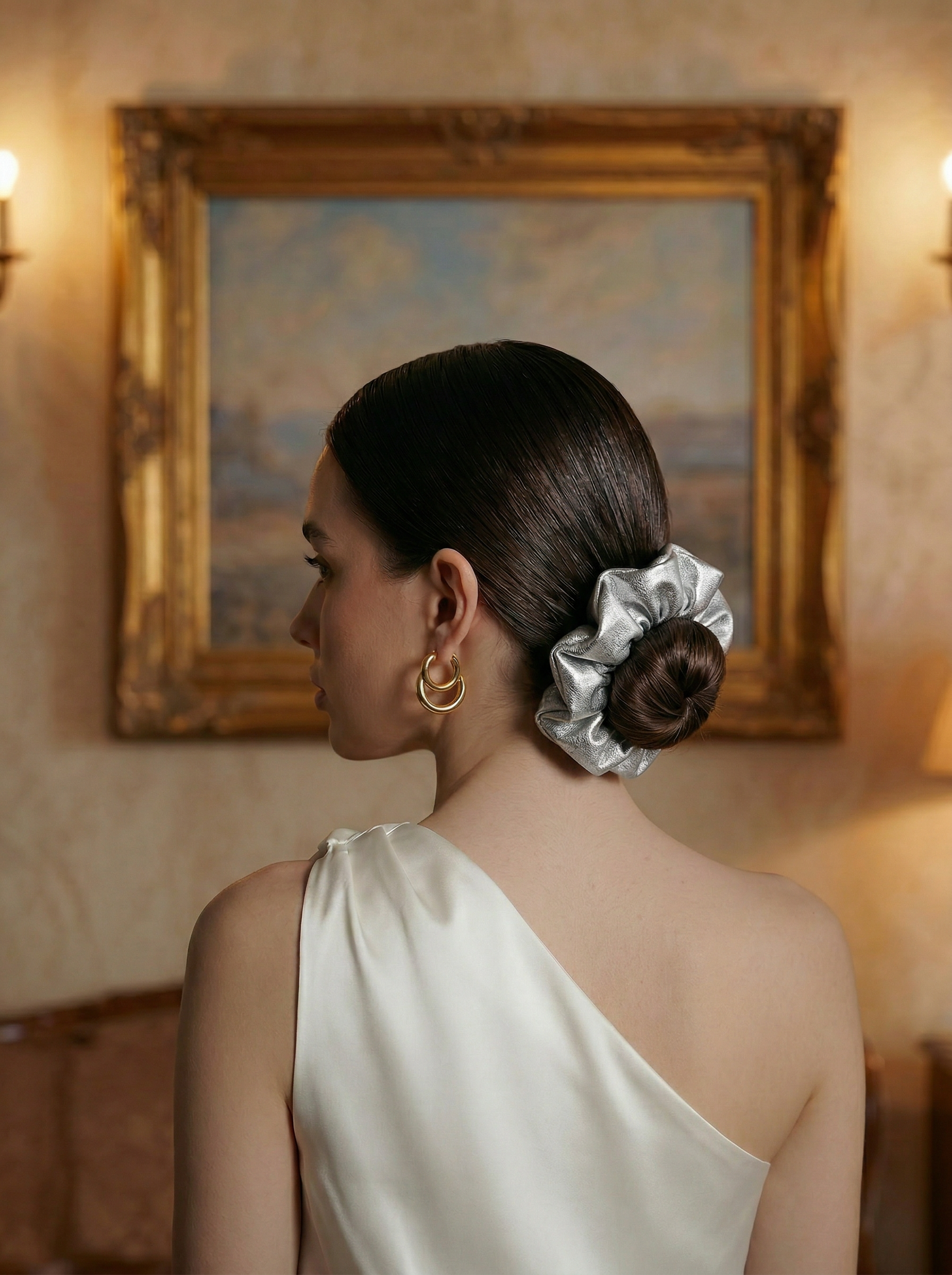 Woman with a silver leather scrunchie in an elegant room with a painting on the wall.