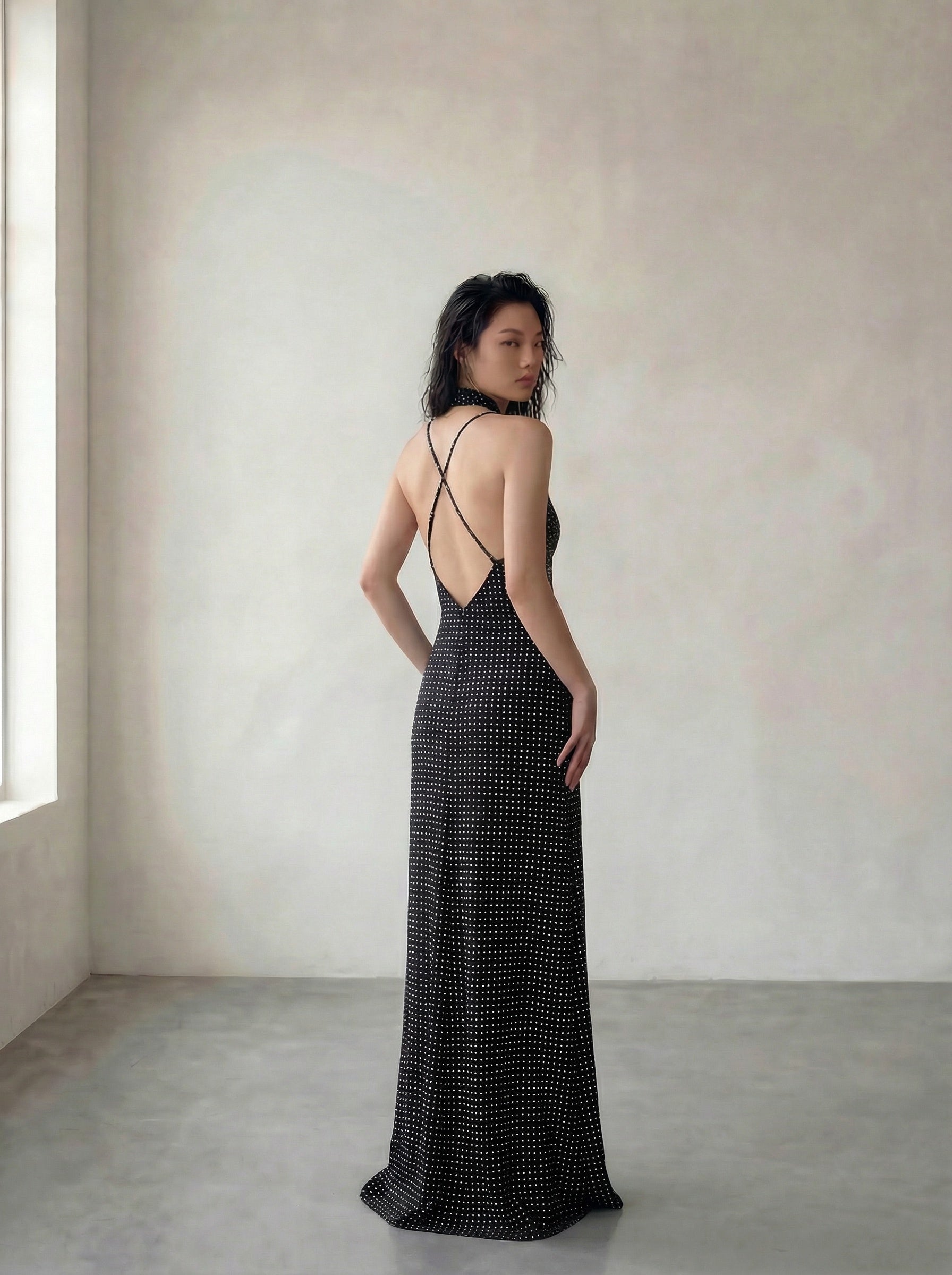 Woman wearing a black polka dot dress with a backless design in a minimalistic setting.