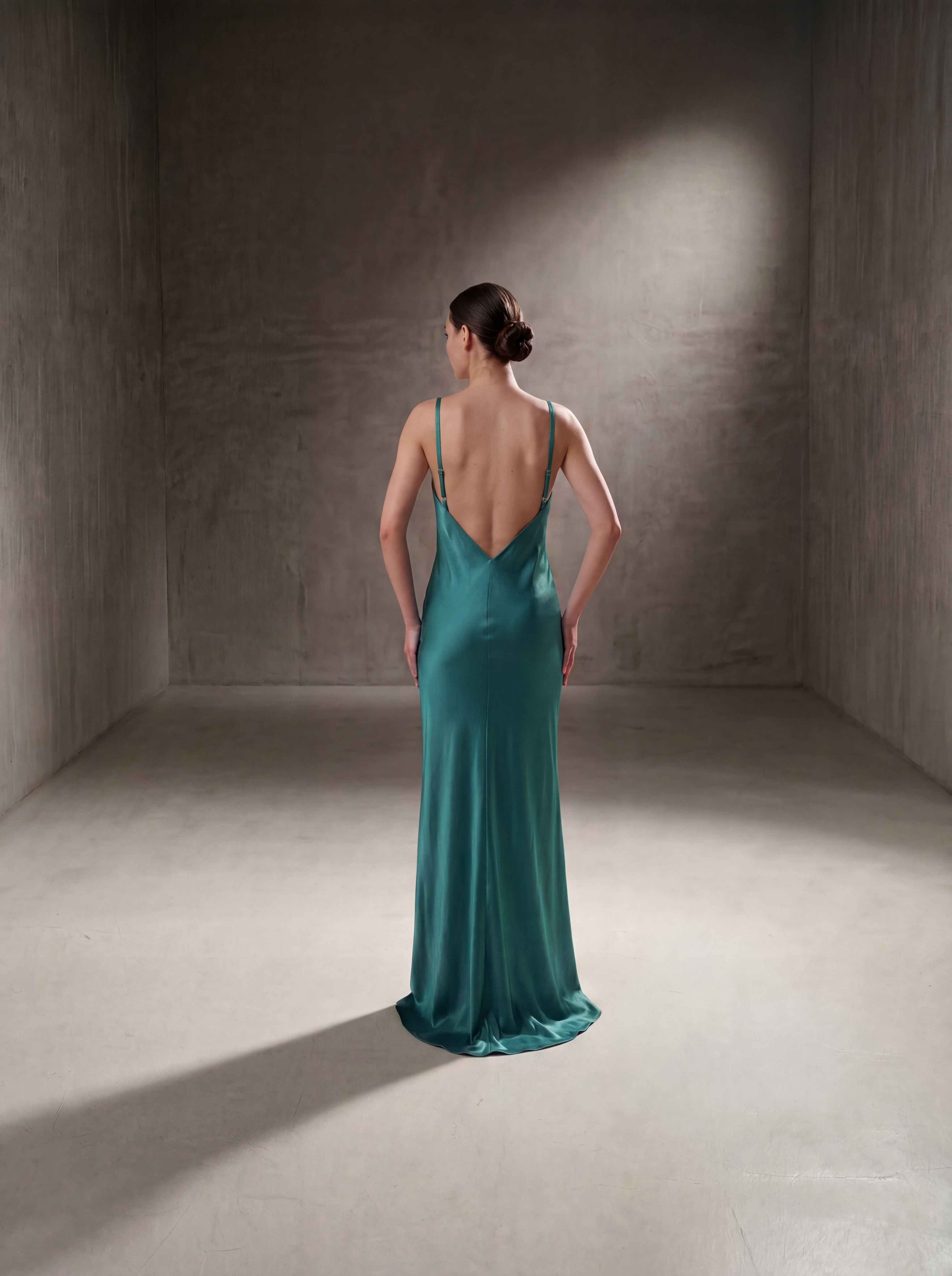Woman in a teal evening gown standing in a dimly lit room with a spotlight on her.