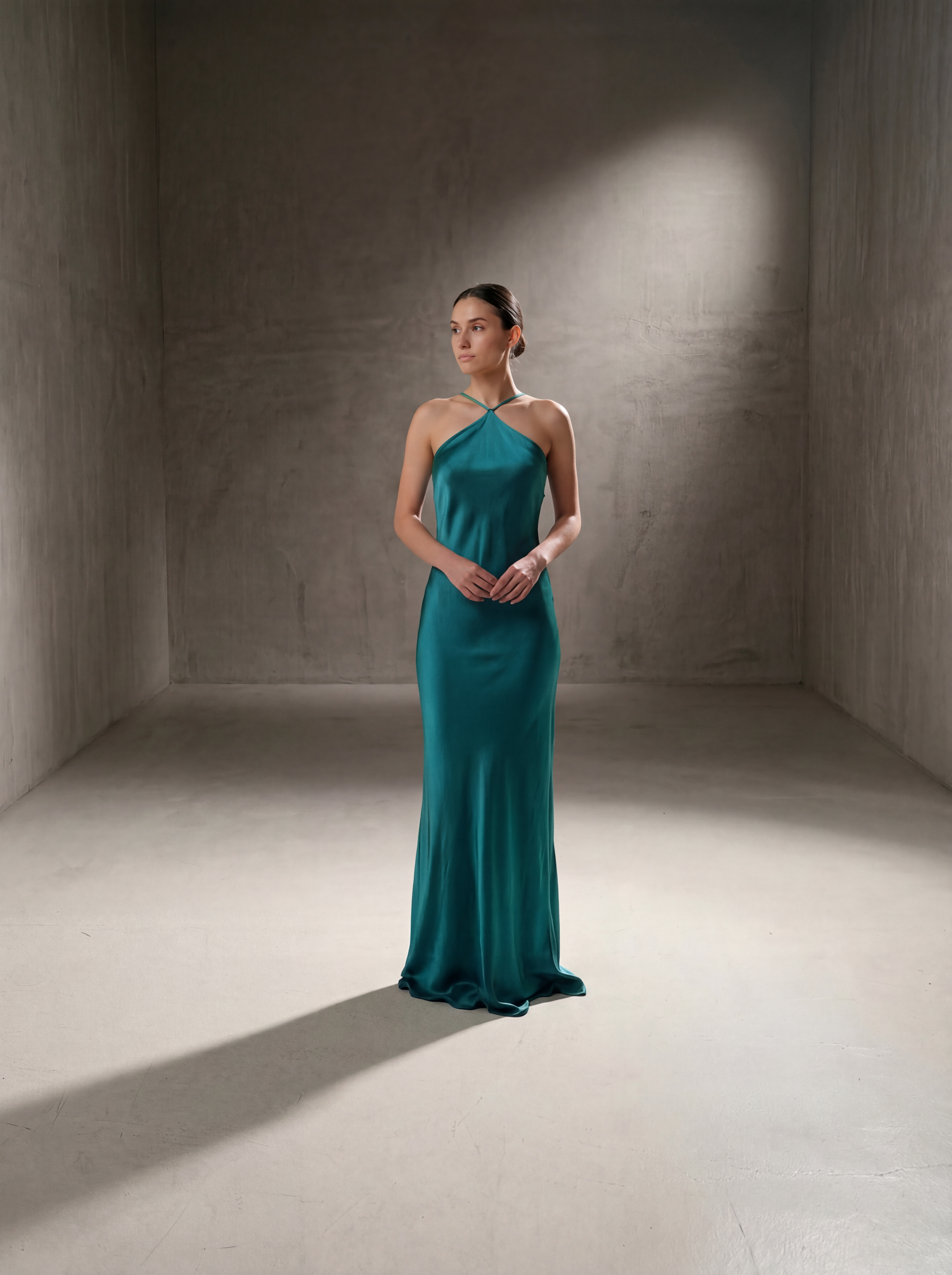 Woman in a teal evening gown standing in a dimly lit room with a spotlight effect.